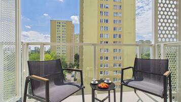 A balcony with two chairs and a small table, overlooking a cityscape with high-rise buildings.