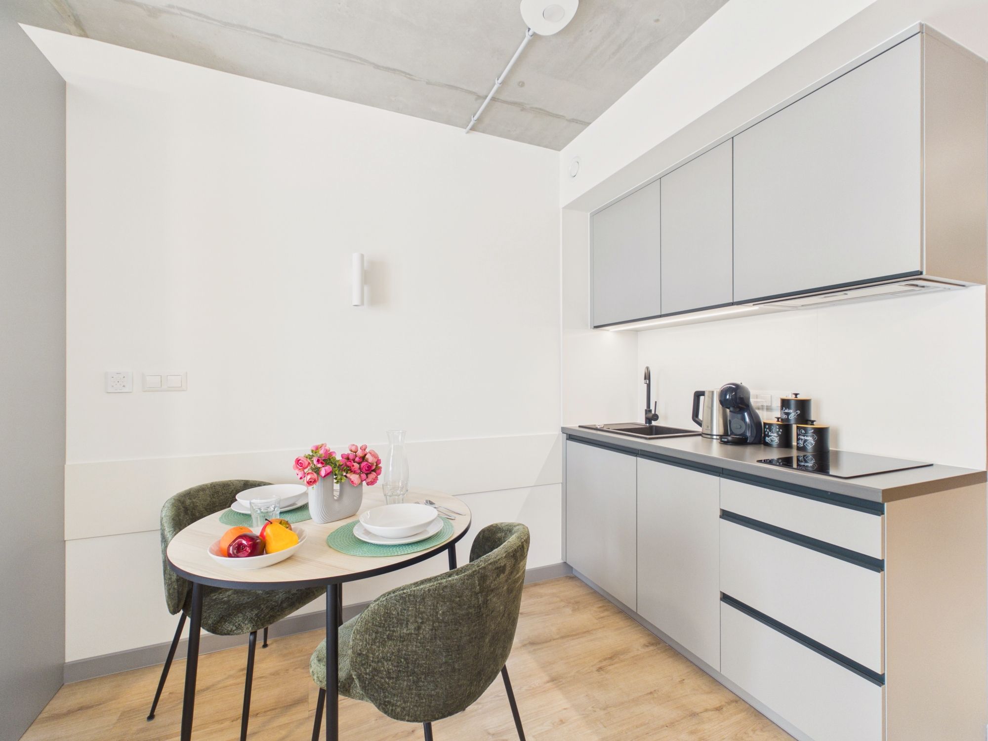 A modern kitchen with white cabinets, a dining table with chairs, and a fruit bowl.