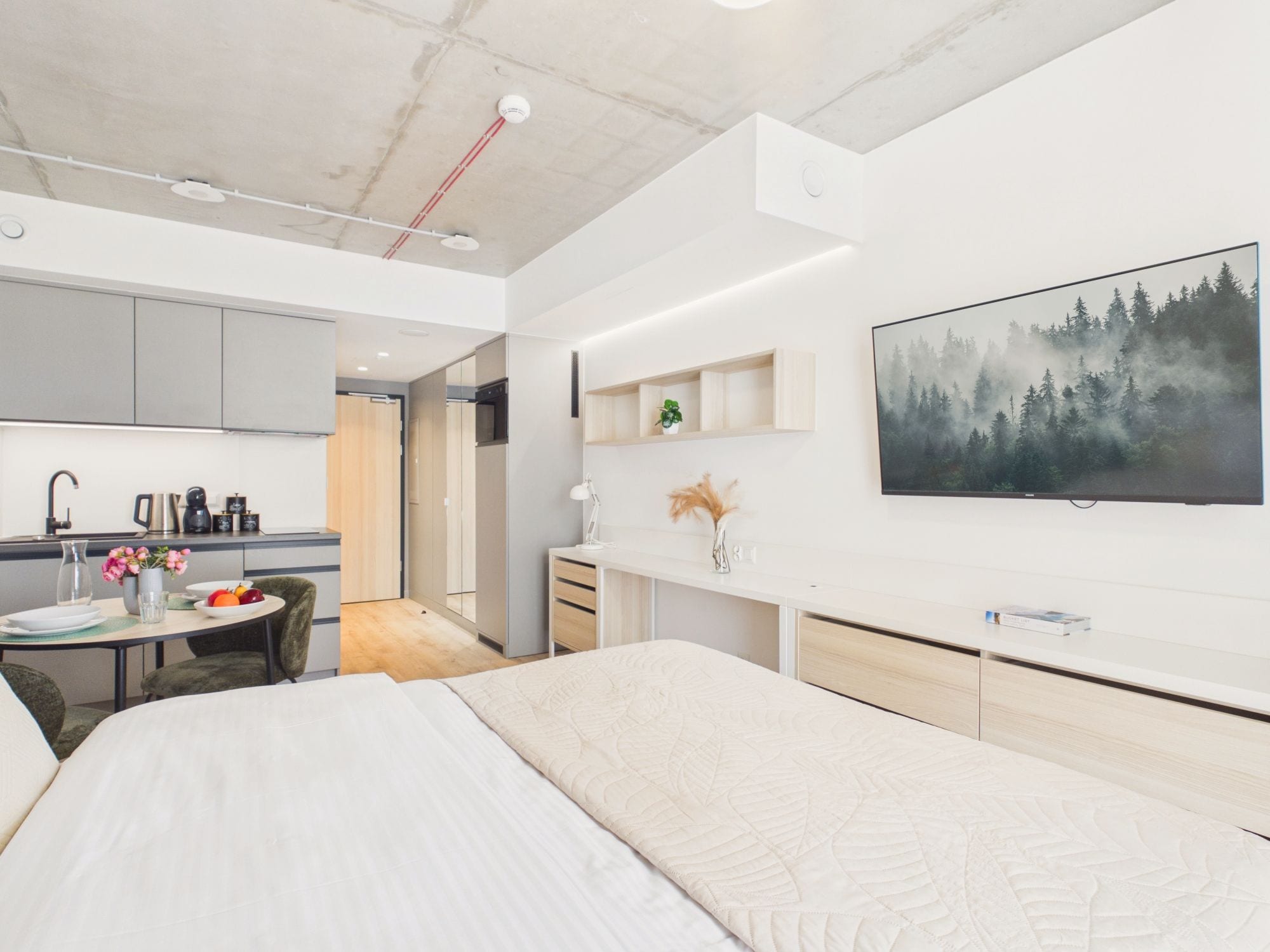 Habitación de hotel moderna con cama, escritorio, silla, kitchenette y un ventanal grande.