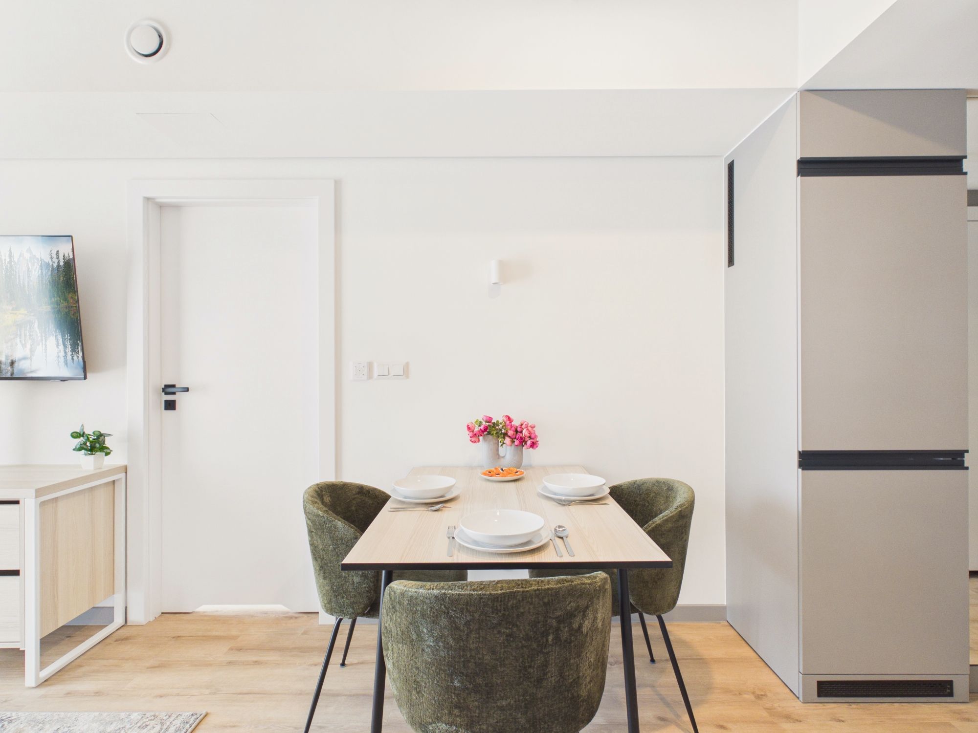 Un comedor moderno con una mesa de madera dispuesta para cuatro personas, rodeada de sillas tapizadas en verde.