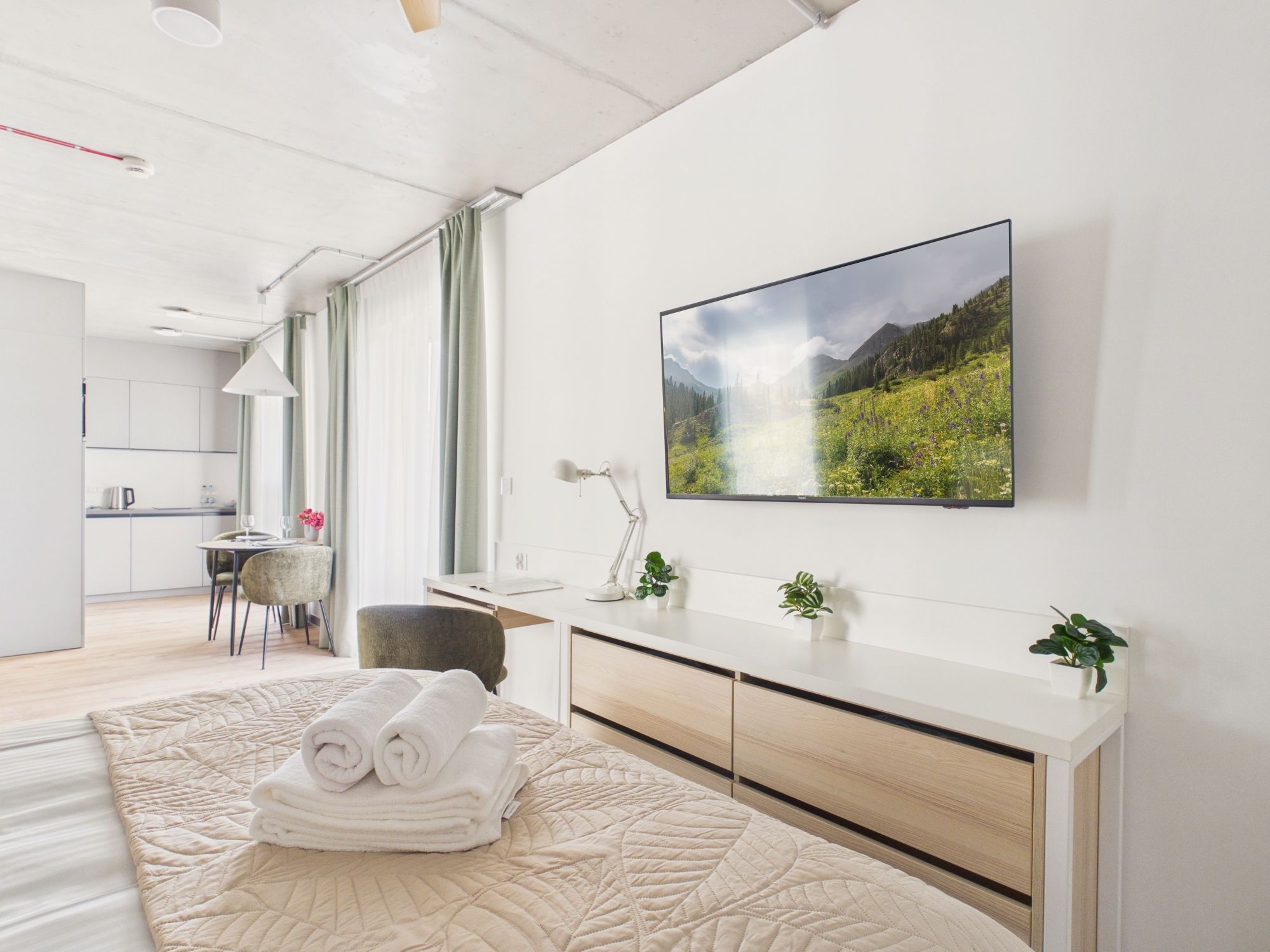 A modern hotel room with a bed, a desk, a chair, a flat-screen TV, and a view of a mountainous landscape.