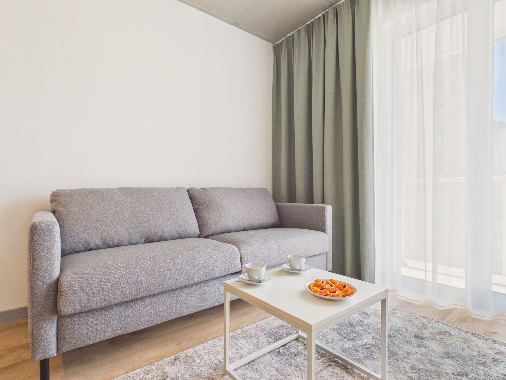 Una sala moderna con un sofá gris, una mesa de centro blanca y una cortina verde.