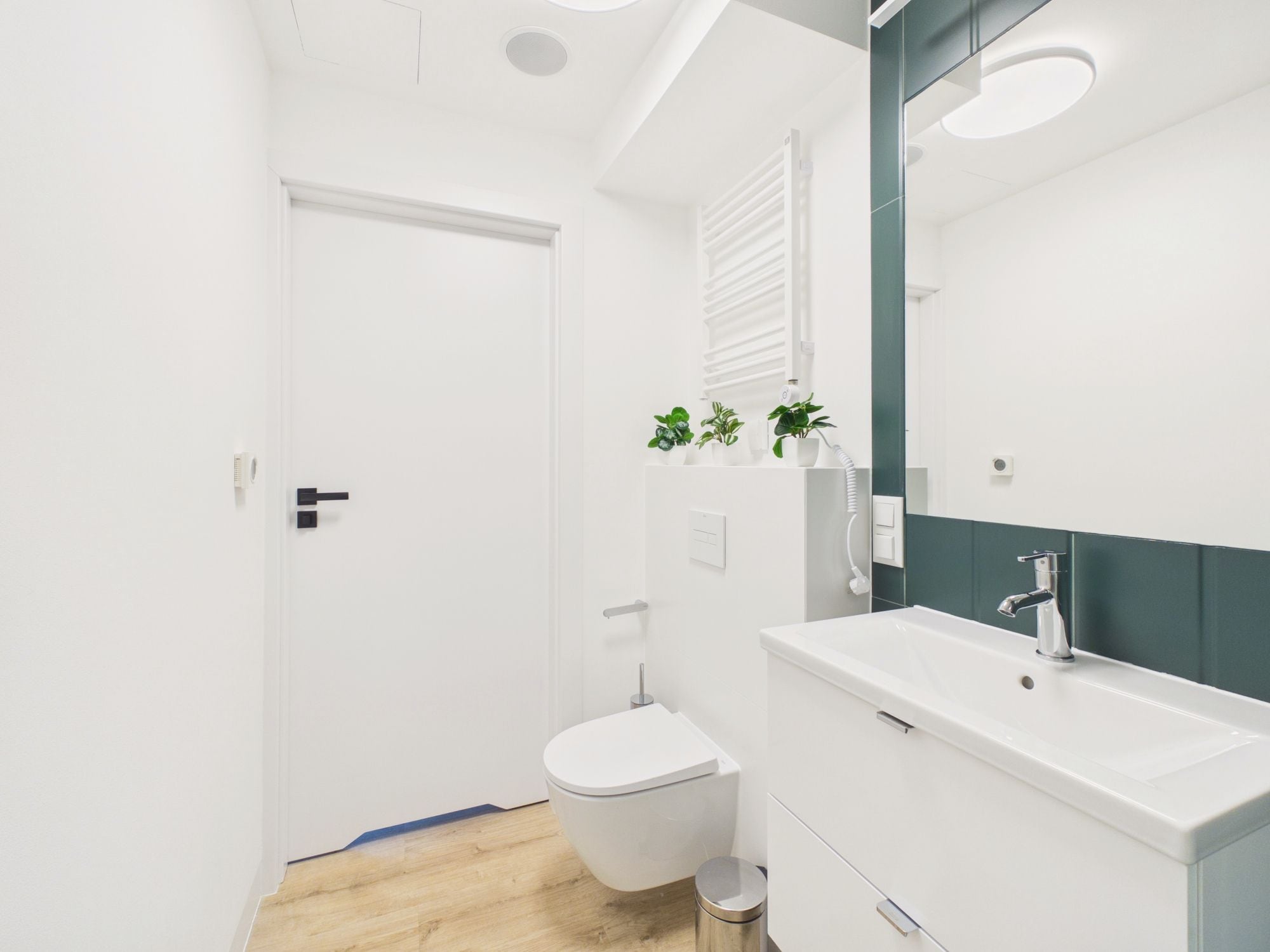 Un baño moderno con un inodoro y un lavamanos blancos, y un espejo con una pared de acento verde.