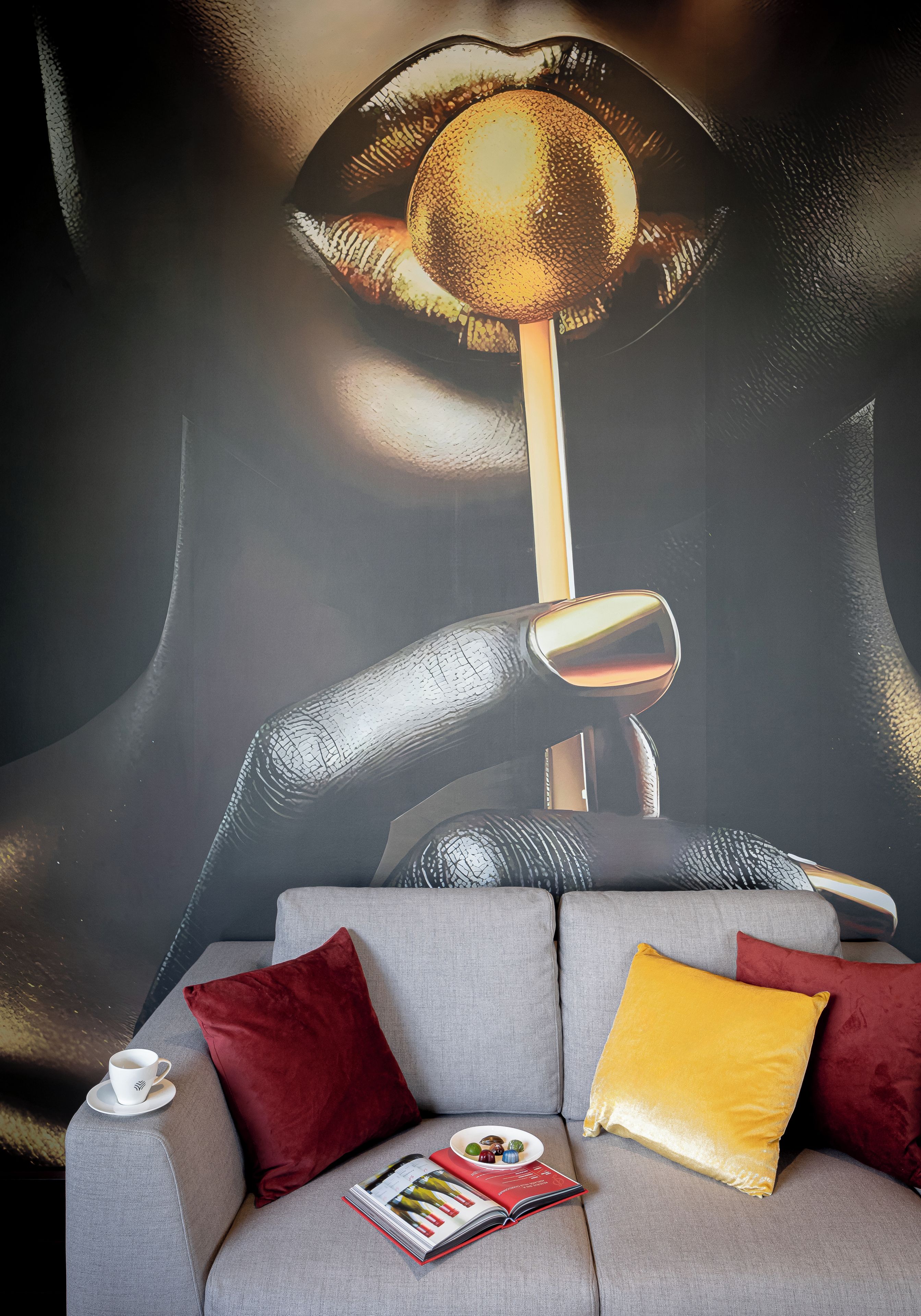 A modern living room with a grey sofa, red and yellow cushions, a white coffee cup, and a magazine.
