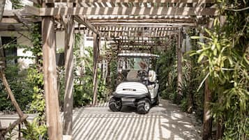 Un vehículo identificado como 'Club Car' circulando por un camino pavimentado bajo una pérgola de madera, con follaje a ambos lados.