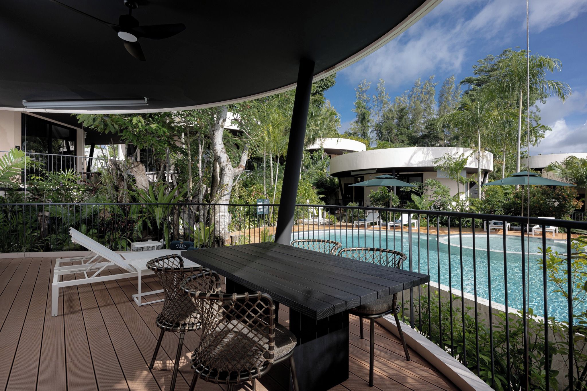A poolside area with a table and chairs, a covered seating area, and a view of a swimming pool.