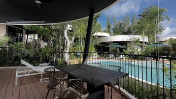 A poolside area with a table and chairs, a covered seating area, and a view of a swimming pool.