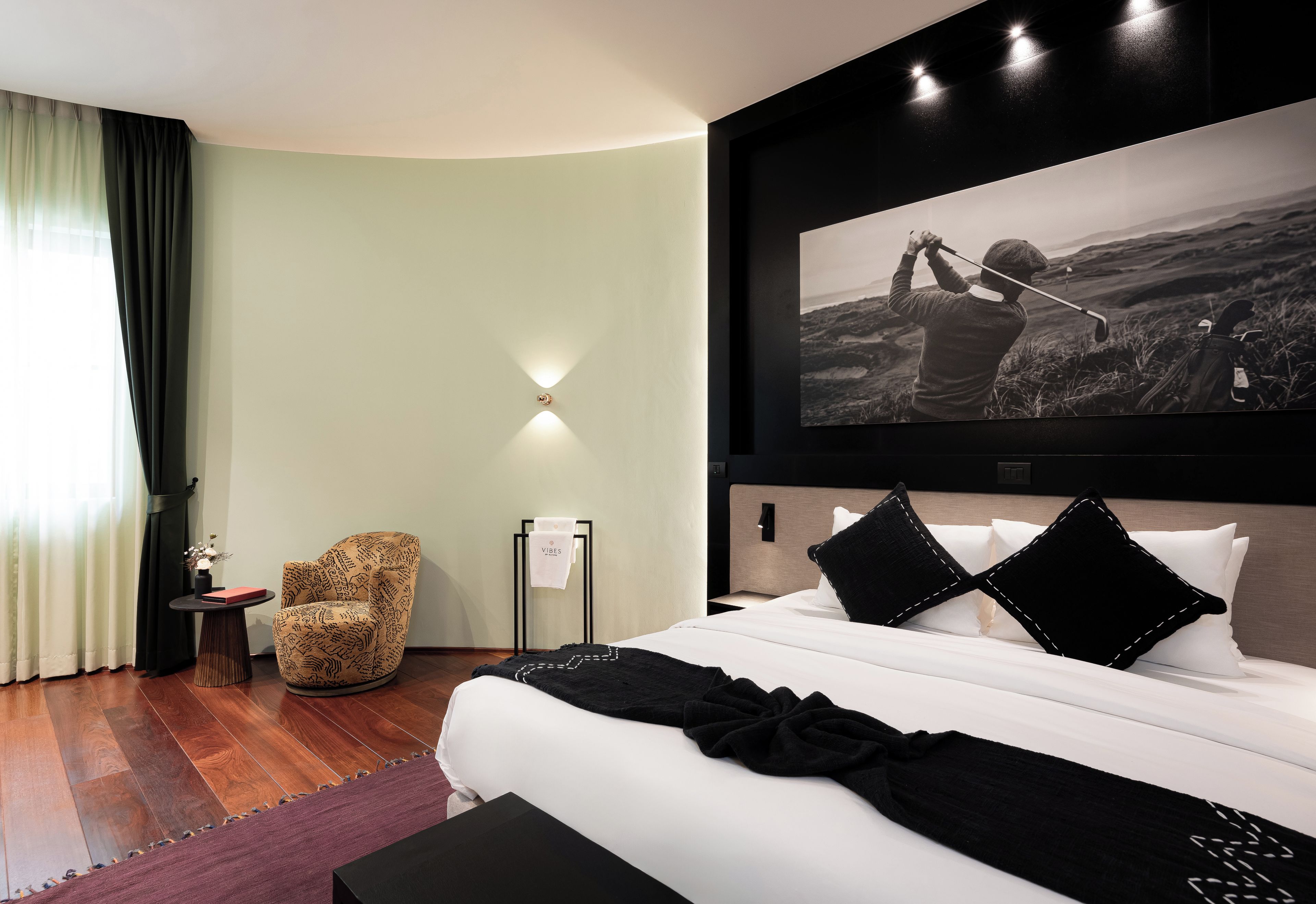 A modern hotel room with a large bed, a chair, a painting, and a view of the outdoors.