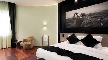 A modern hotel room with a large bed, a chair, a painting, and a view of the outdoors.