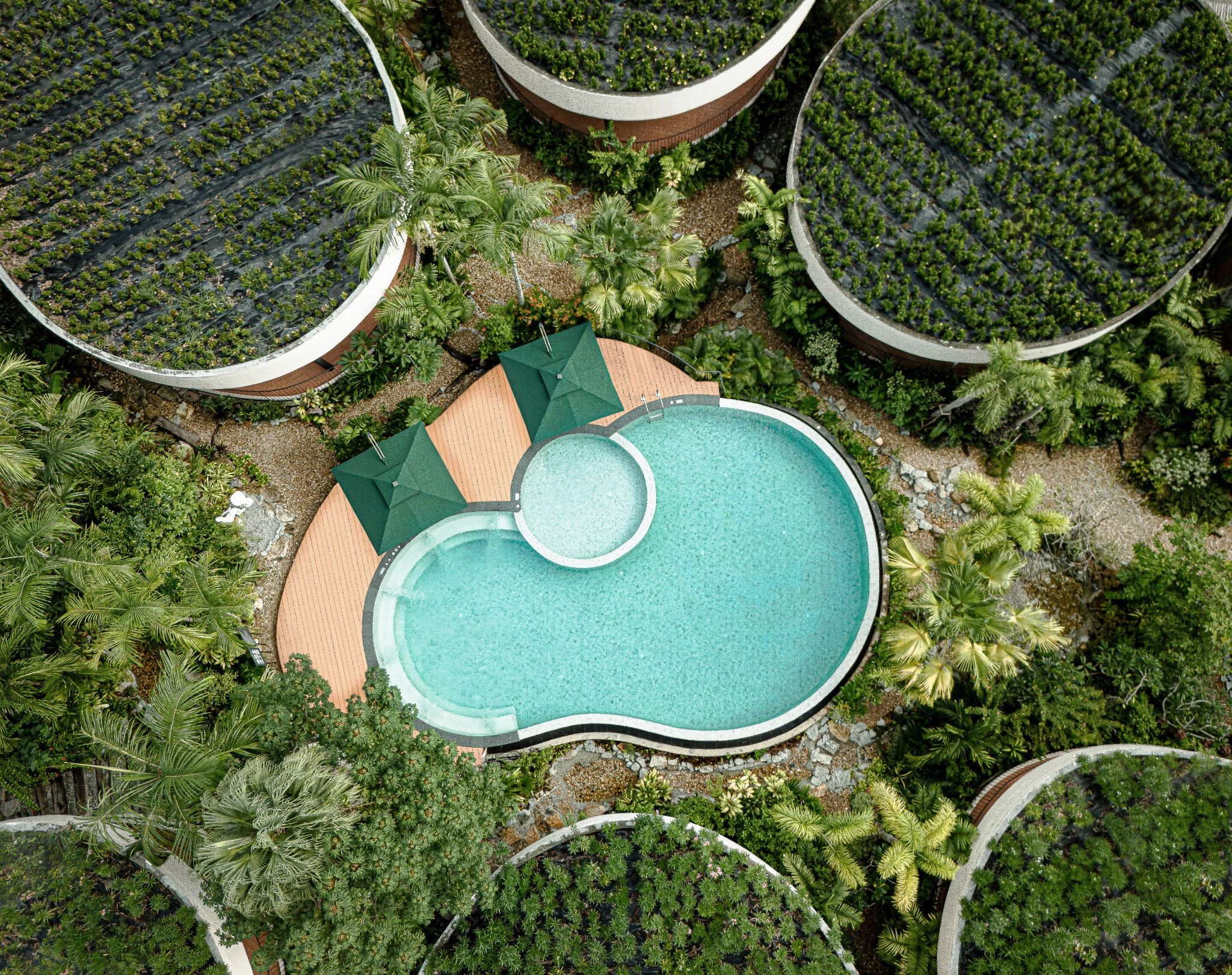 An aerial view of a resort with a central swimming pool surrounded by lush greenery and multiple circular water features.