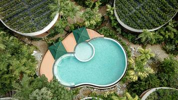 An aerial view of a resort with a central swimming pool surrounded by lush greenery and multiple circular water features.