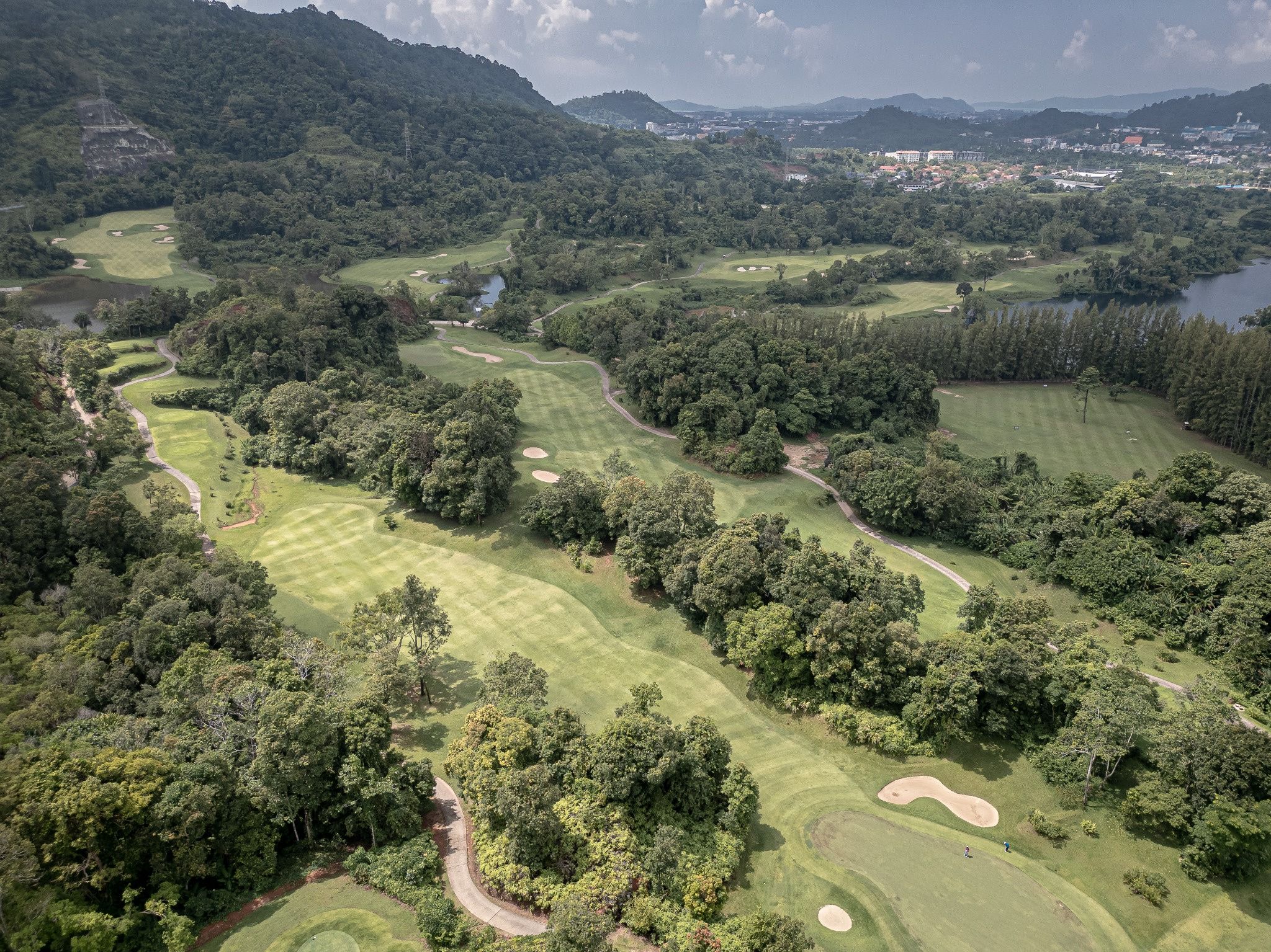 An aerial view of a golf course with multiple fairways, sand bunkers, and water hazards.