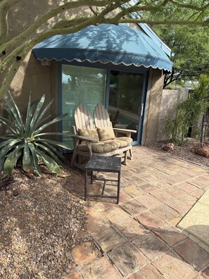 A patio with two Adirondack chairs, a small table, and a blue awning over a glass door. - Come for the Quiet......Stay for the Luxurious Amenities and the convenience (Apache Junction)