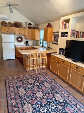 A kitchen with wooden cabinets, a white refrigerator, a dining area with two chairs, a rug, and a bookshelf with books. - Come for the Quiet......Stay for the Luxurious Amenities and the convenience (Apache Junction)