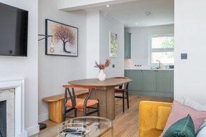 A modern living room with a fireplace, a dining table with chairs, a TV mounted on the wall, and a kitchen in the background. - Wimbledon Village Duplex, Near Tennis Club (London)