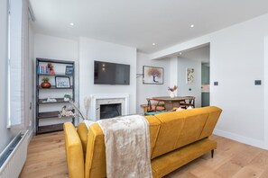 A modern living room with a sofa, a fireplace, a dining table, and a bookshelf. - Wimbledon Village Duplex, Near Tennis Club (London)