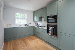 A modern kitchen with light green cabinets, a wooden countertop, a window, and a built-in oven. - Wimbledon Village Duplex, Near Tennis Club (London)