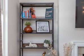 A bookshelf with books, a framed picture, a vase, and a decorative sign. - Wimbledon Village Duplex, Near Tennis Club (London)