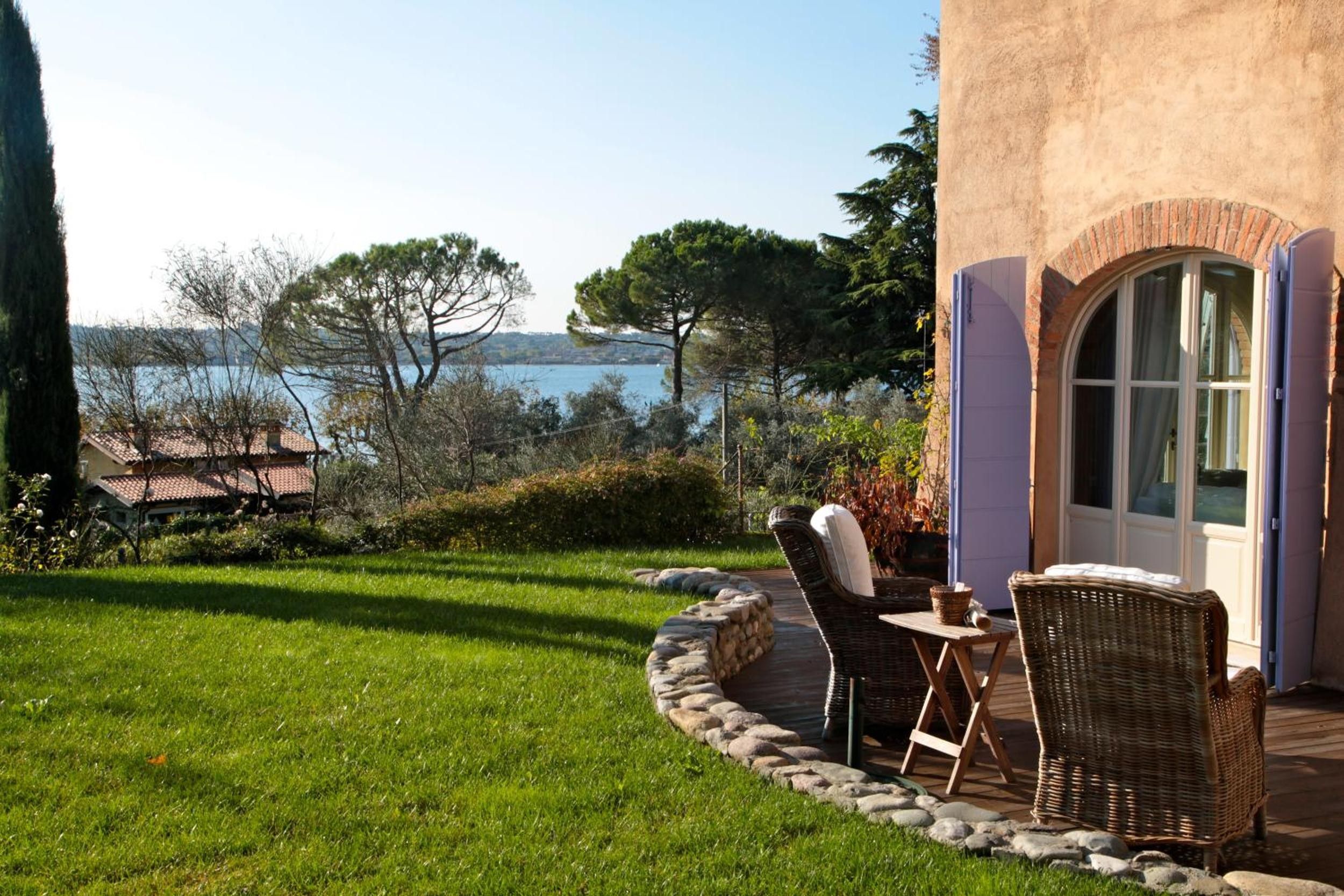 Eine Terrasse mit Korbmöbeln und einer Steinbordüre, mit Blick auf ein Gewässer und Bäume.