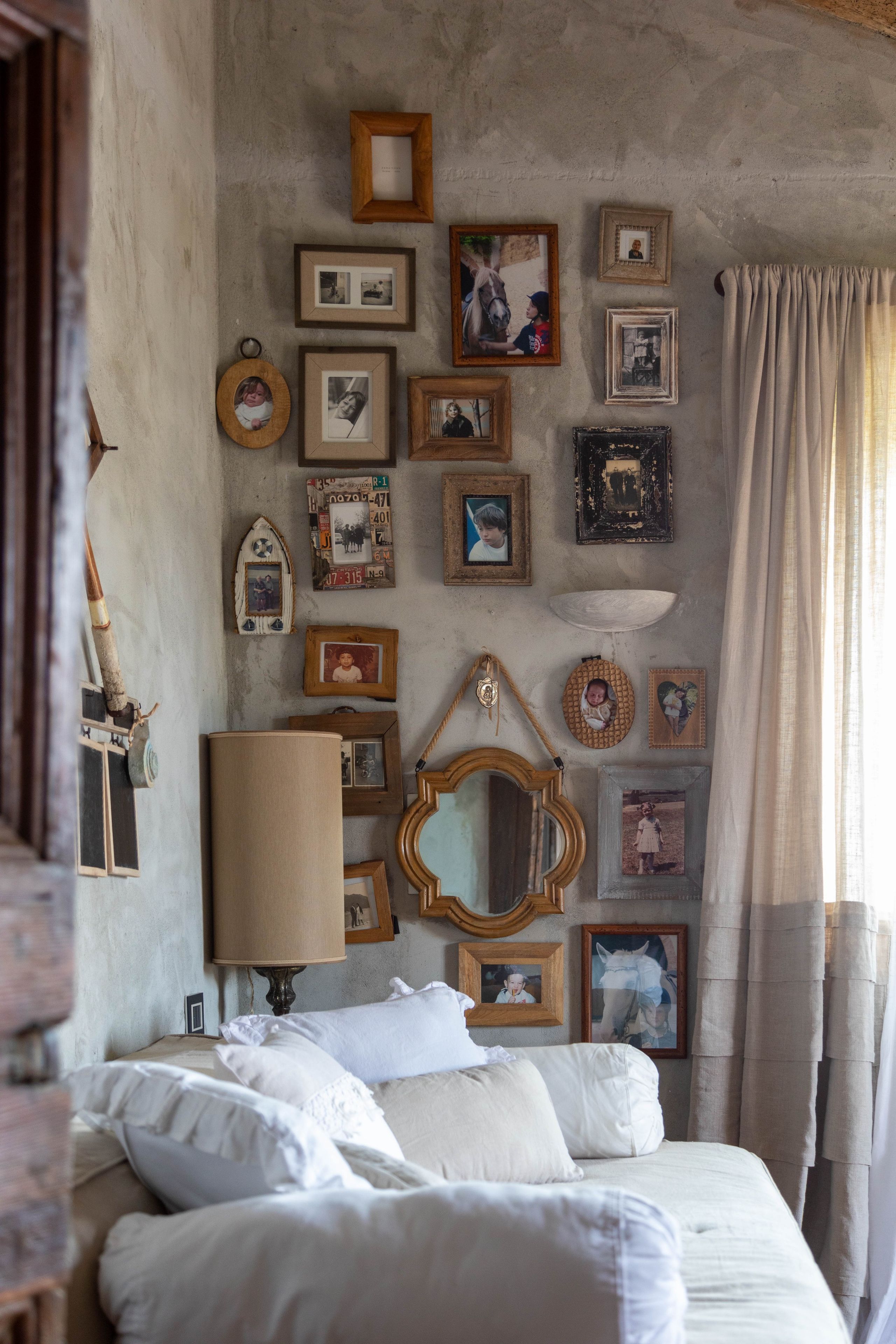 A bedroom with a bed, pillows, a mirror, and various framed pictures on the wall.