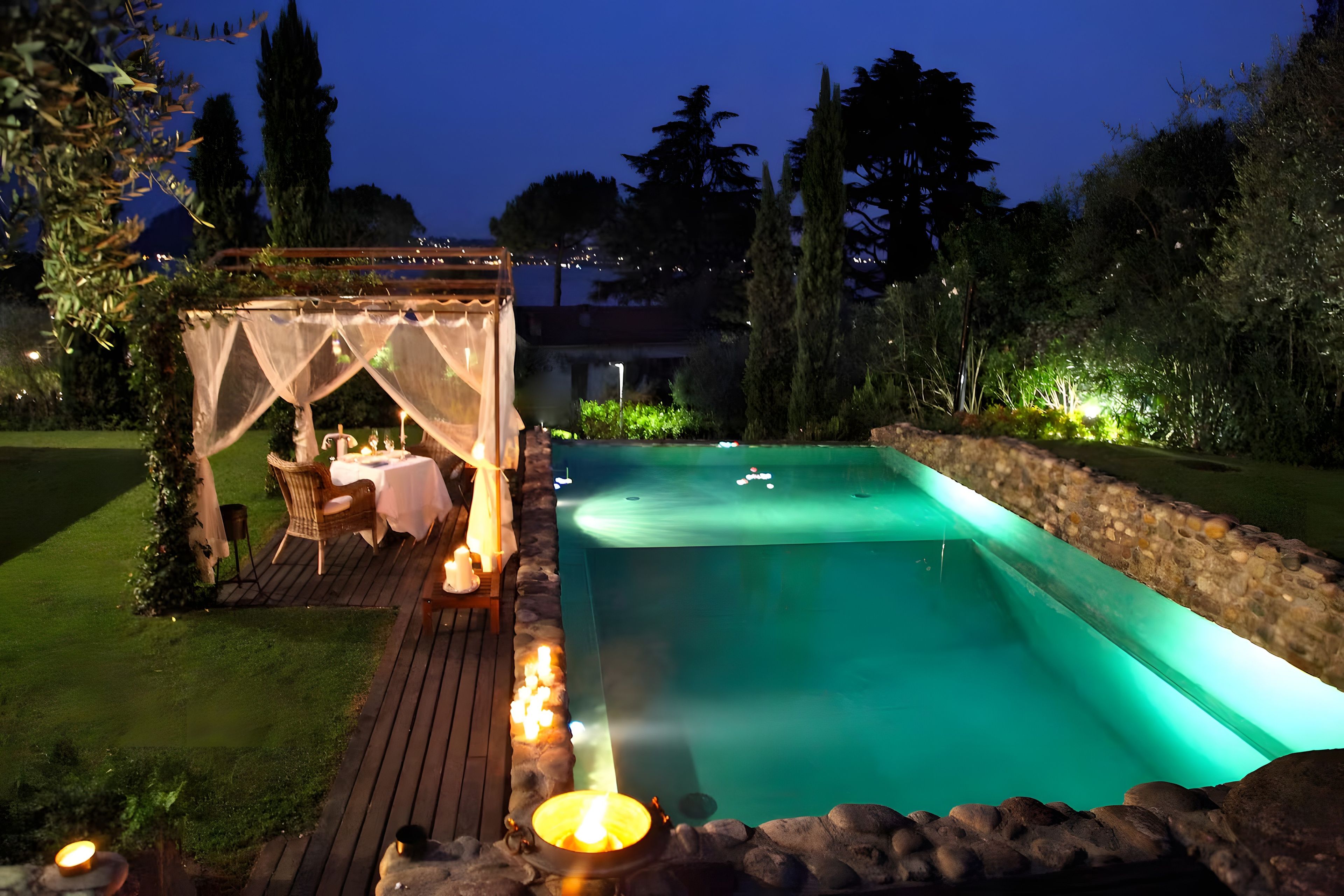 A pool area with a wooden deck, a covered seating area, and a stone wall.