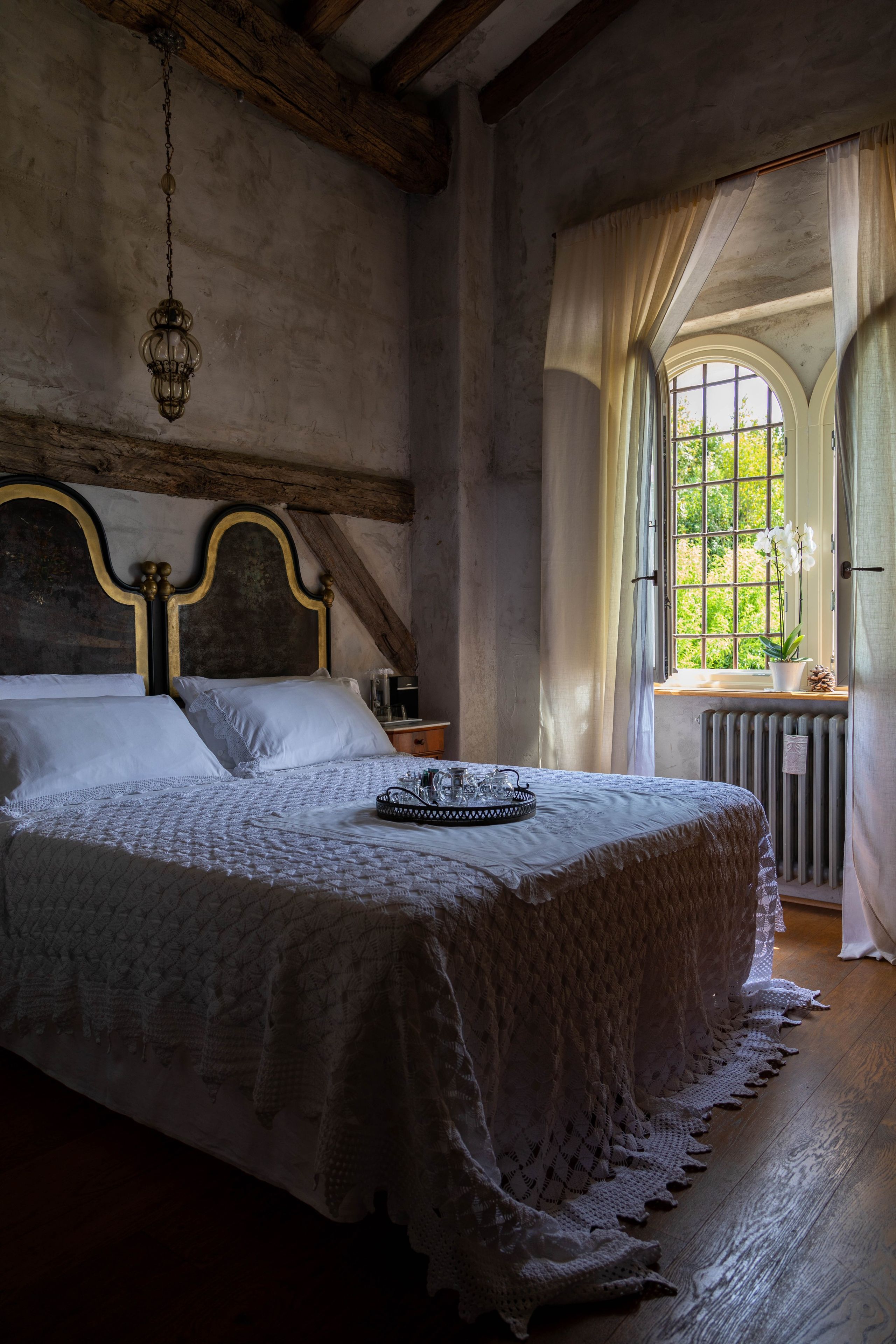 Ein Schlafzimmer mit einem großen Bett, einer Hängelampe, einem Fenster mit Vorhängen und einer Heizung.