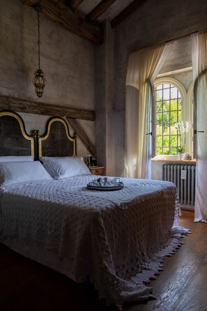 Un dormitorio con una cama grande, una lámpara colgante, un ventanal con cortinas y un radiador.