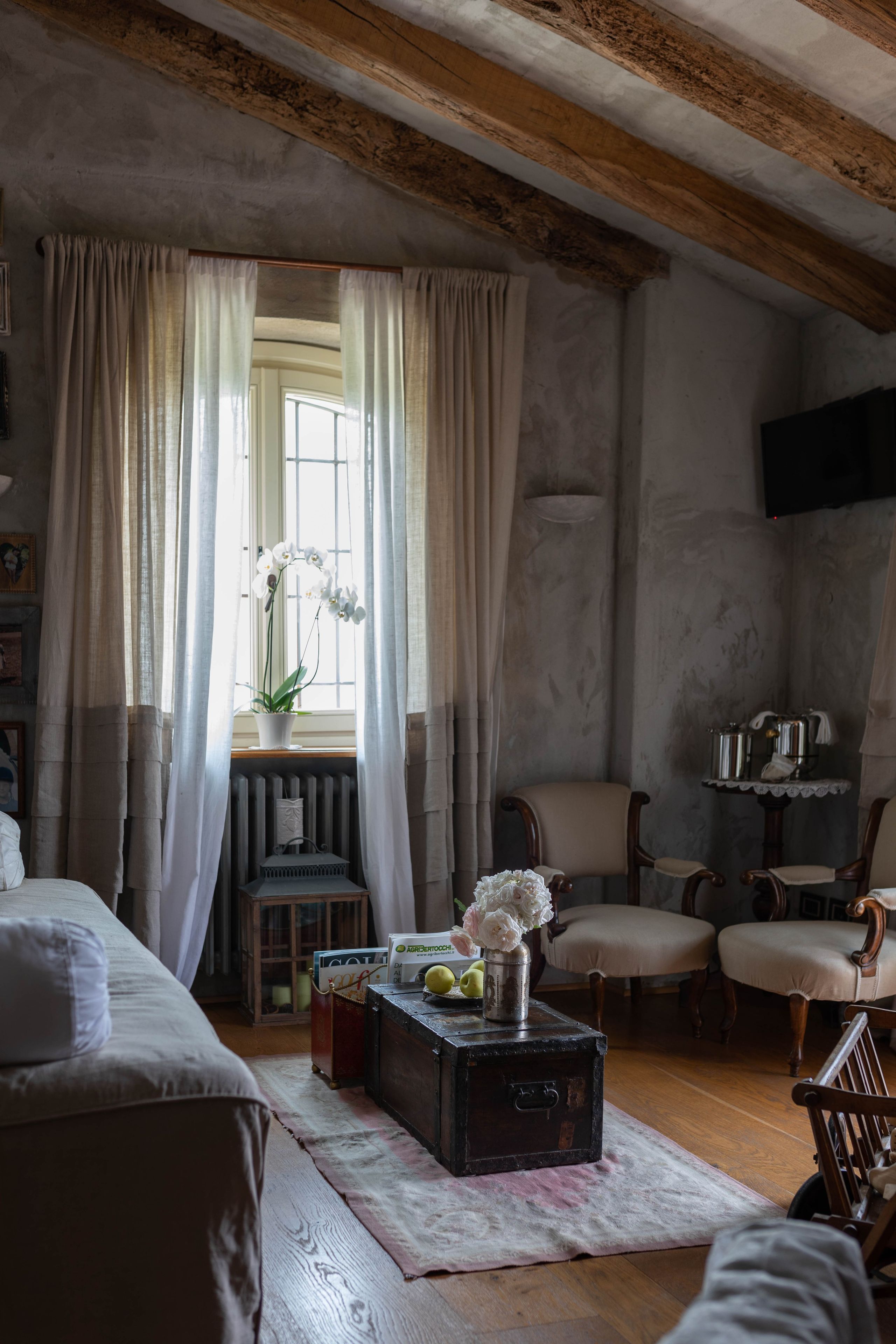 Ein gemütliches Zimmer mit einem Bett, einer Holzablage, einem Tisch mit Blumen und einem fenster mit Vorhängen.