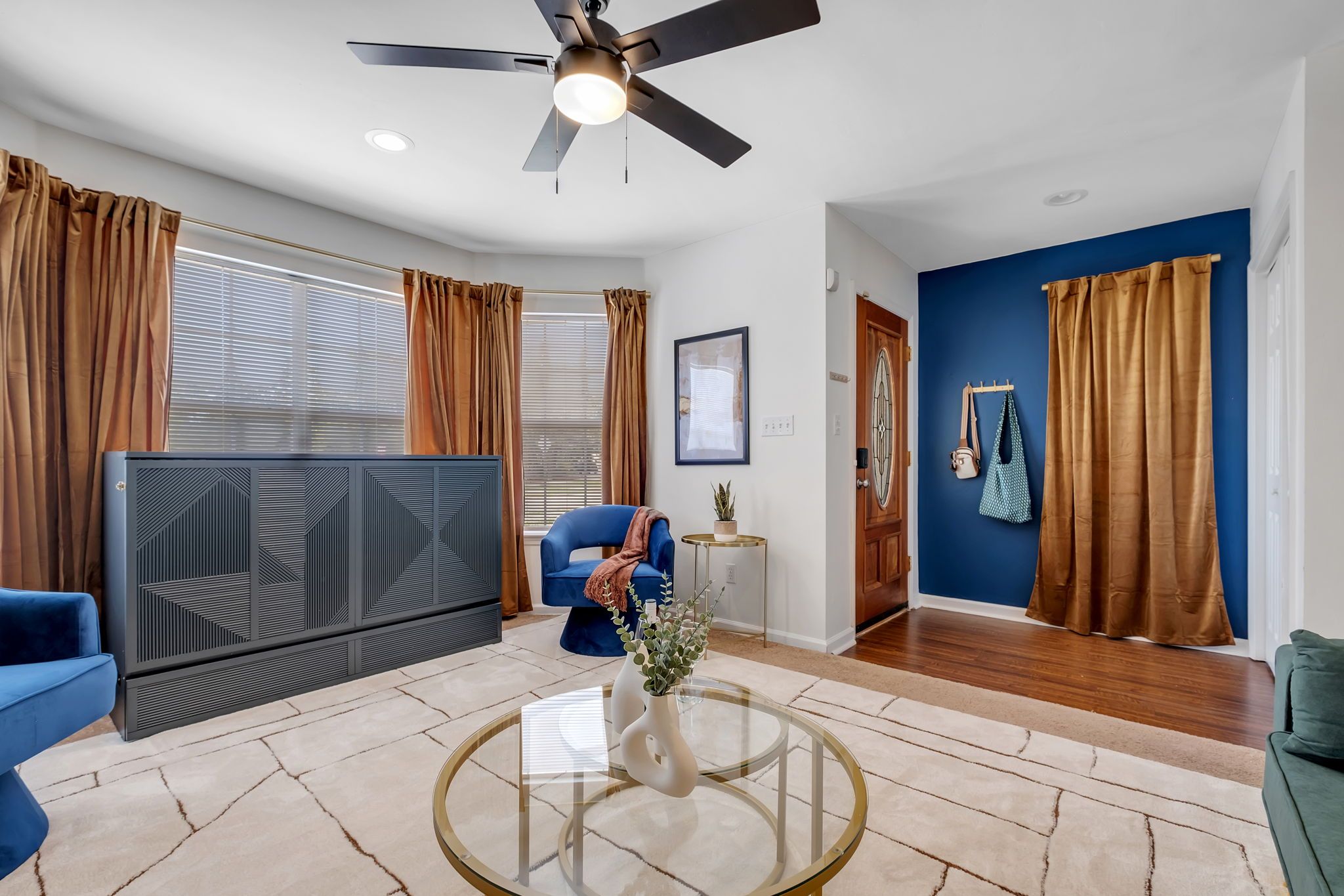 A modern living room with a blue sofa, a glass coffee table, a ceiling fan, and a large radiator.