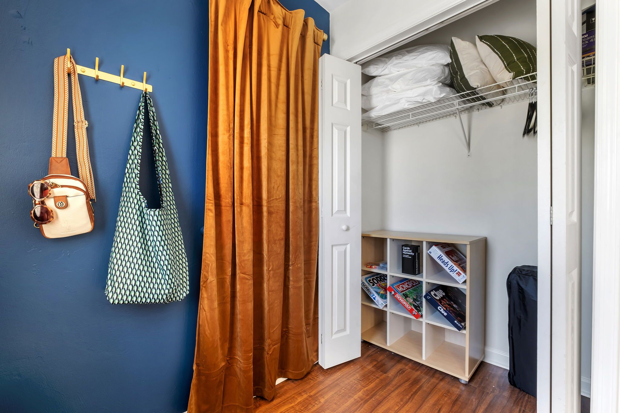 A room with a blue wall, a wooden door, a brown curtain, a hanging bag, and a bookshelf with magazines.