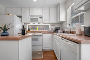 Una cocina moderna con muebles blancos, un microondas integrado, una estufa y un lavavajillas.