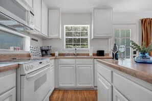 Una cocina moderna con armarios blancos, horno empotrado y ventana con persianas.