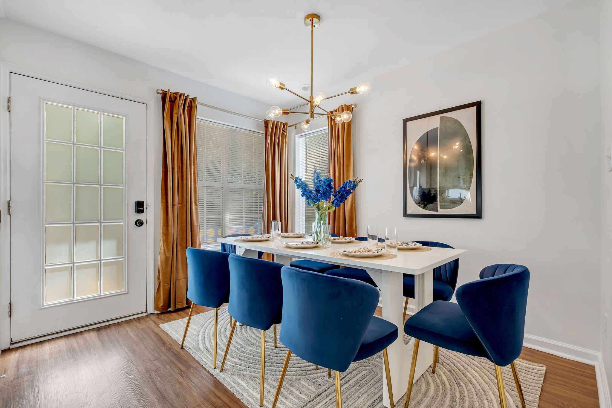 A dining area with a white table, blue chairs, a chandelier, and a vase with blue flowers.