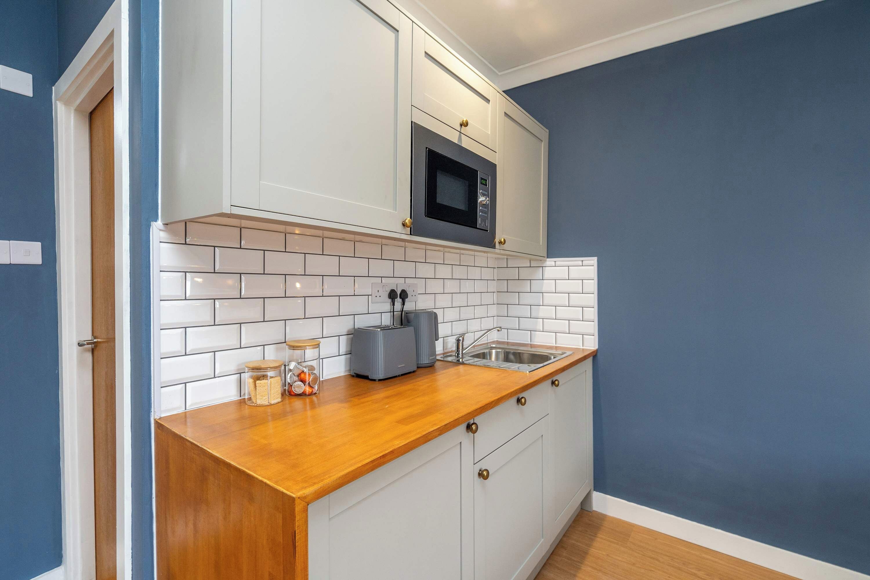 A kitchen with white cabinets, a wooden countertop, a microwave, a toaster, and a sink.