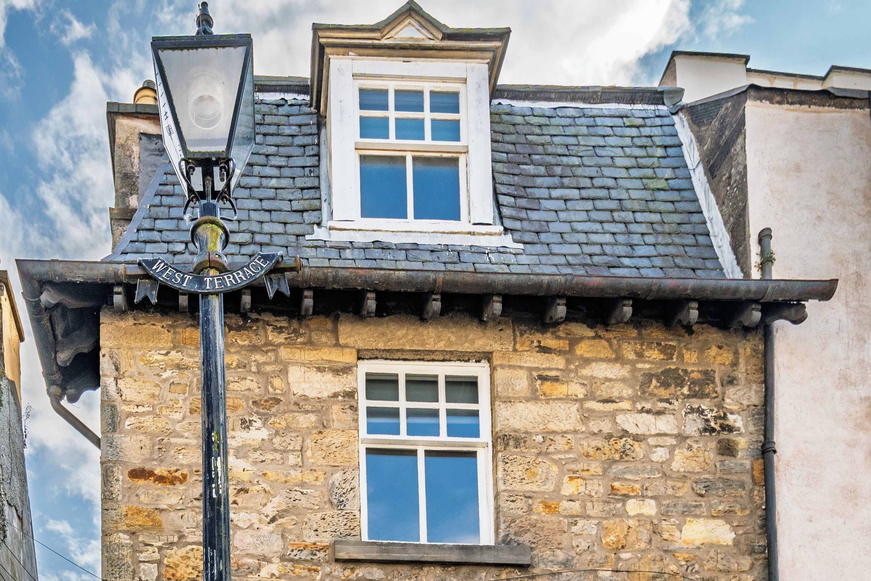Un bâtiment en pierre à l’architecture traditionnelle, doté d’une petite fenêtre et d’un lampadaire avec une enseigne.