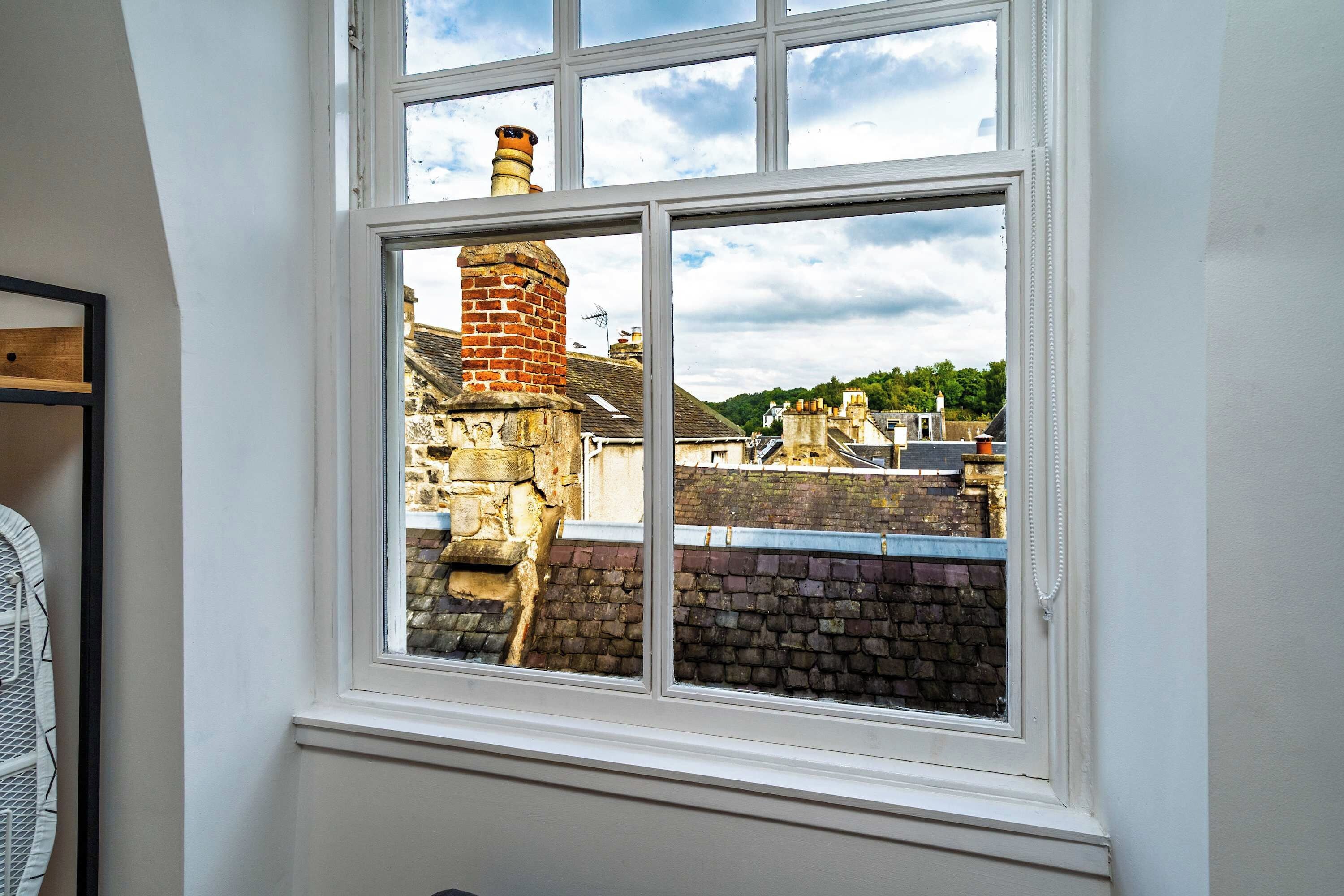 A window with a view of a brick chimney and a stone wall.