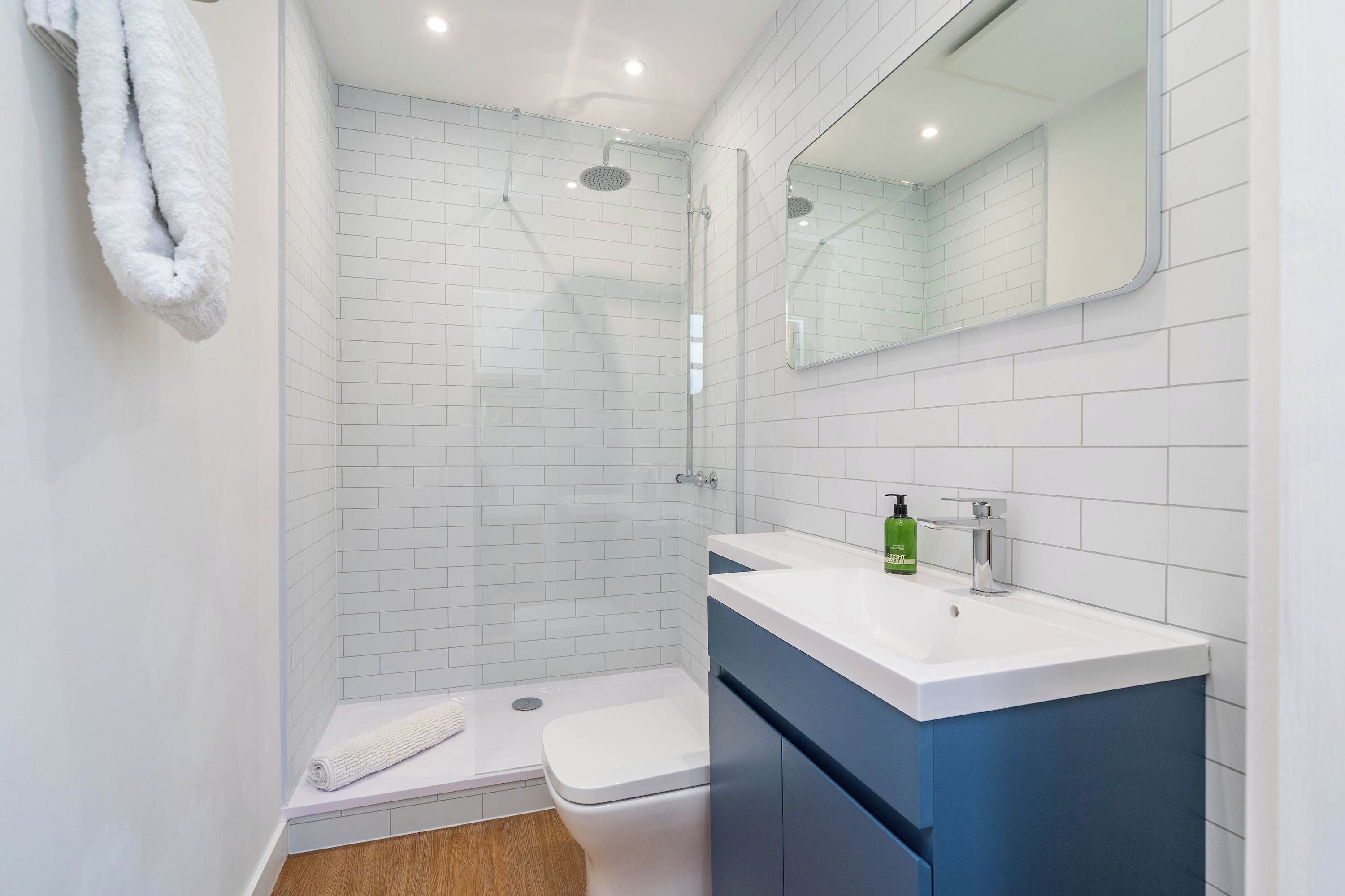 Un bany modern amb una dutxa de vidre, un lavabo blanc amb un moble blau i un mirall sobre el lavabo.