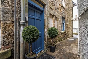A stone building with a blue door and two potted topiary plants. - Cozy Studio at The Brewery (Queensferry)