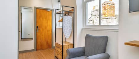 A modern room with a grey armchair, wooden wardrobe, and a window with a view of a brick building.