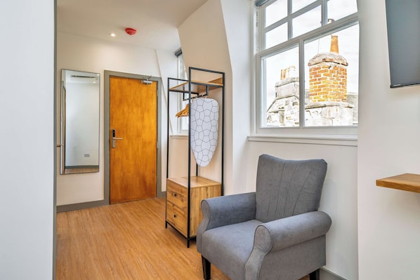 A modern room with a grey armchair, wooden wardrobe, and a window with a view of a brick building. - Cozy Studio at The Brewery (Queensferry)