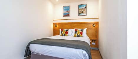 A hotel room with a bed, a headboard, two wall-mounted pictures, and a ceiling light.