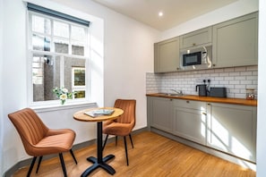 A compact kitchen with a microwave, a sink, and a window with a view of a building. There are two chairs and a small table with a magazine. - Cozy Studio at The Brewery (Queensferry)