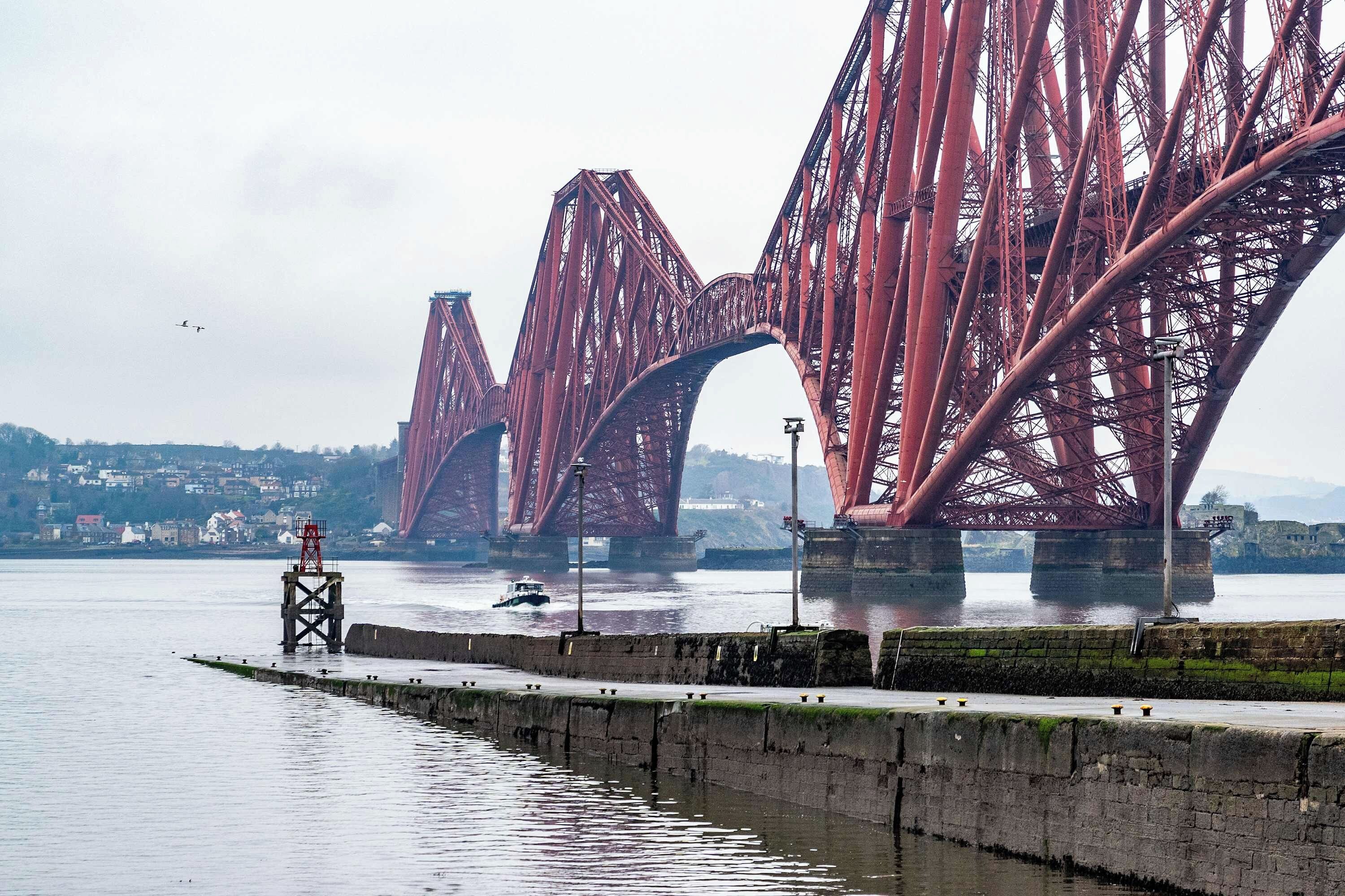 A large red steel bridge spanning a body of water with a small boat in the foreground.