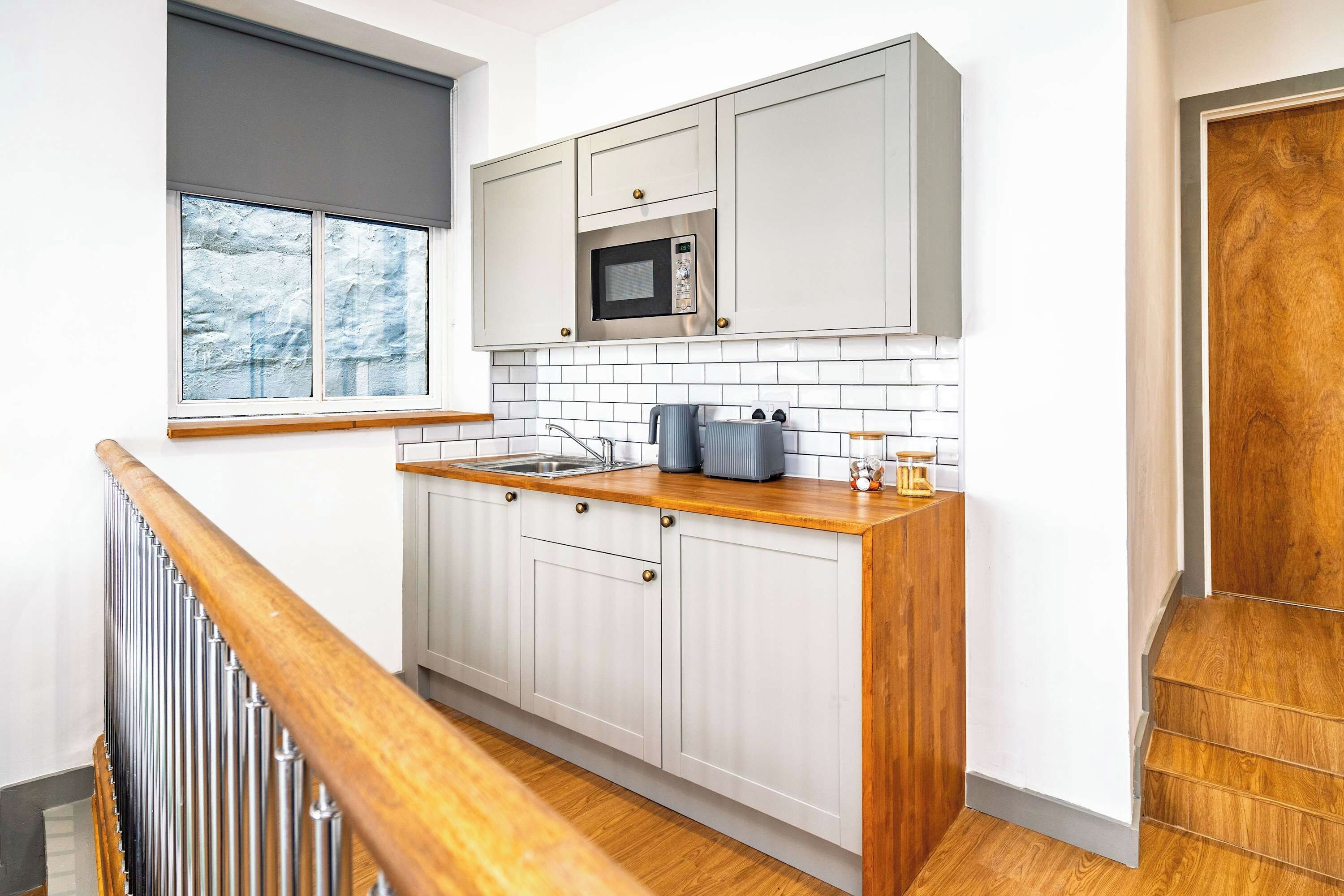 A kitchen with white cabinets, a microwave, a sink, and a wooden countertop.