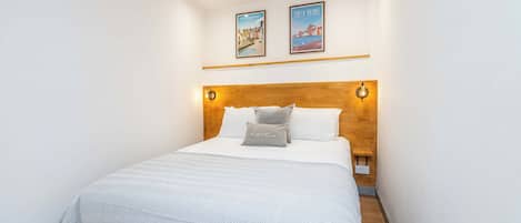 A hotel room with a bed, a wooden headboard, two wall-mounted light fixtures, and two framed pictures above the bed.