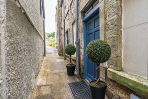 A narrow alleyway with stone walls, a blue door, and two potted topiary trees. - Elegant Studio at The Brewery (Queensferry)