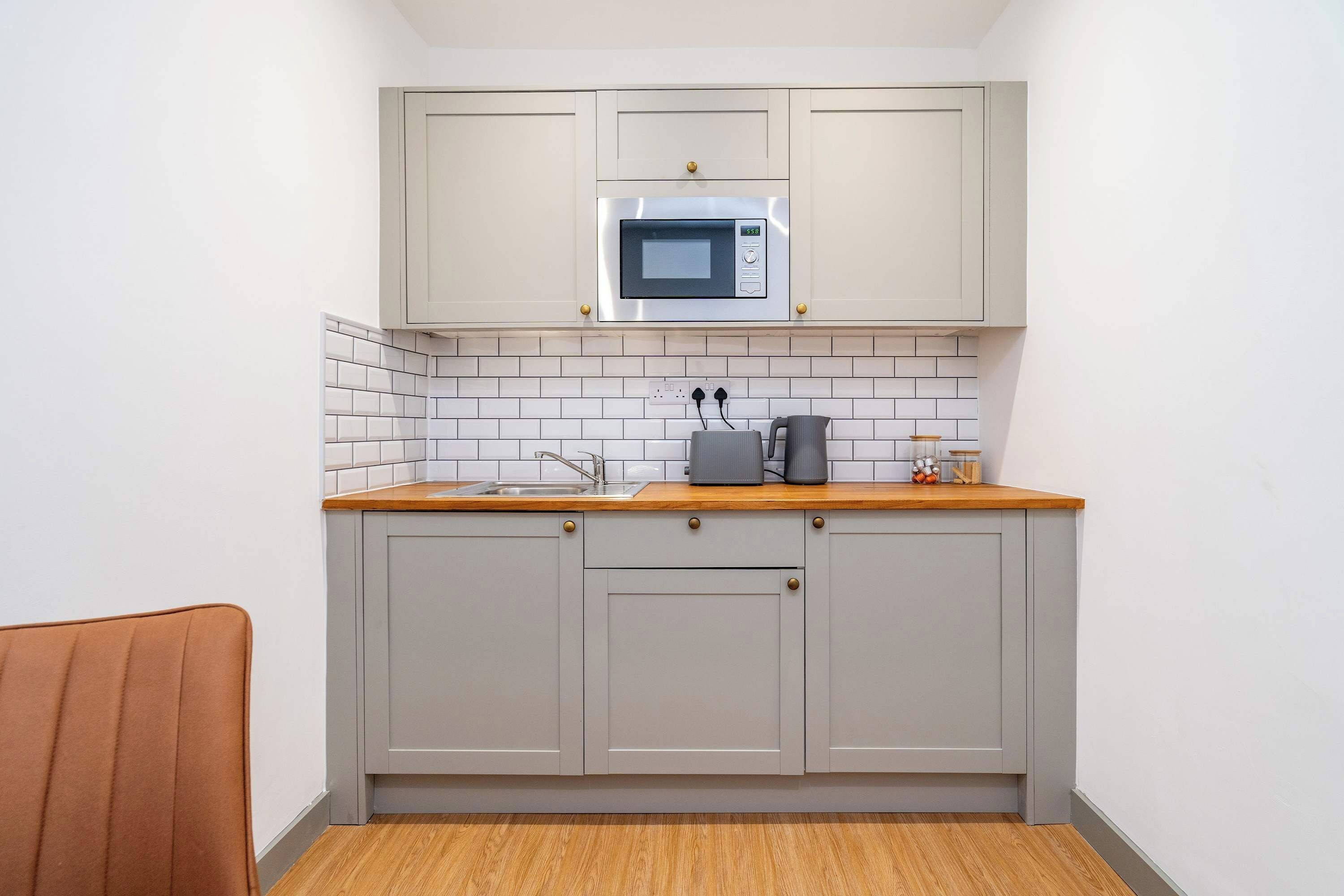 A compact kitchen with a microwave, a kettle, and a coffee maker on the countertop.