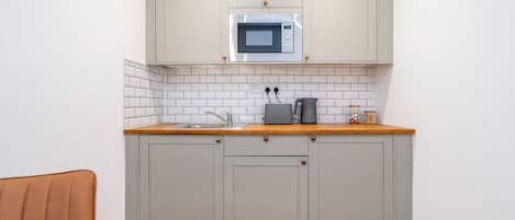 A compact kitchen with a microwave, a kettle, and a coffee maker on the countertop.