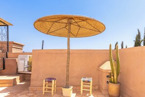 A patio with a woven umbrella, two wooden chairs, a potted cactus, and a white refrigerator. - Elegant 3-bedroom Riad with AC perfect for relaxing stays (Marrakech)