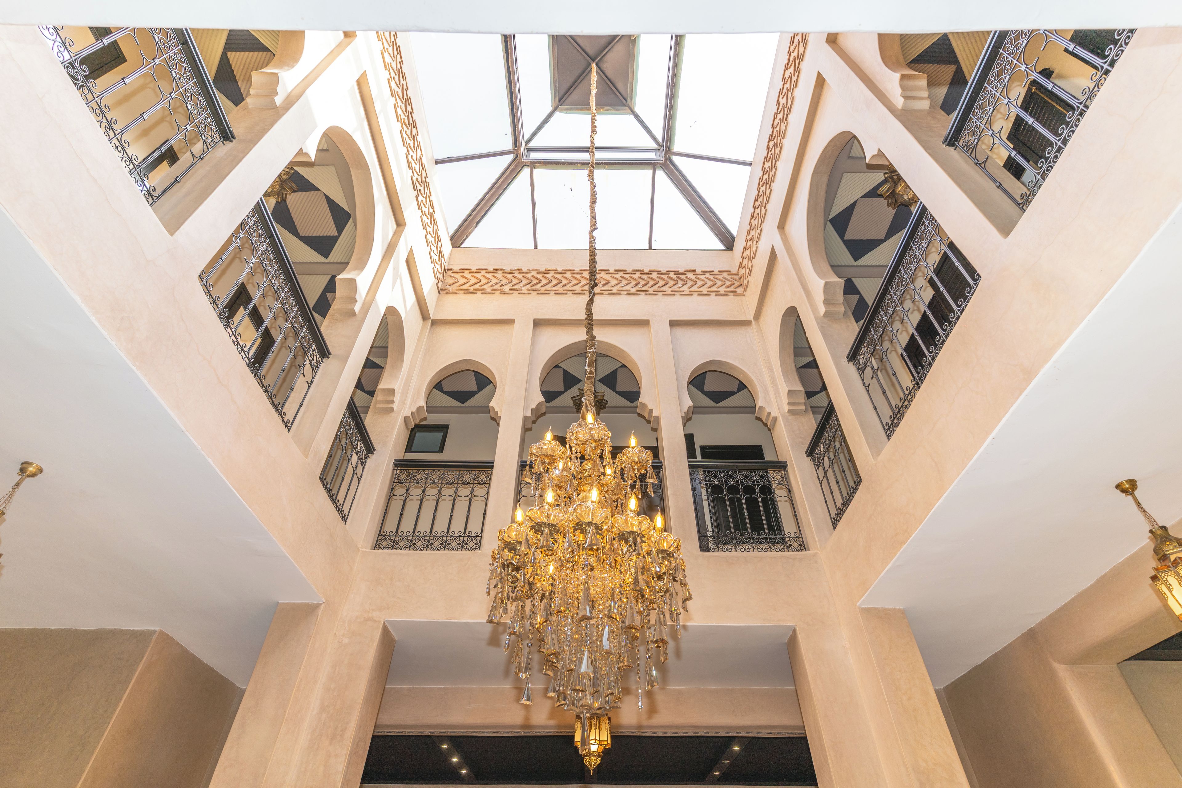 A grand interior with a large chandelier, arched windows, and intricate metal railings.